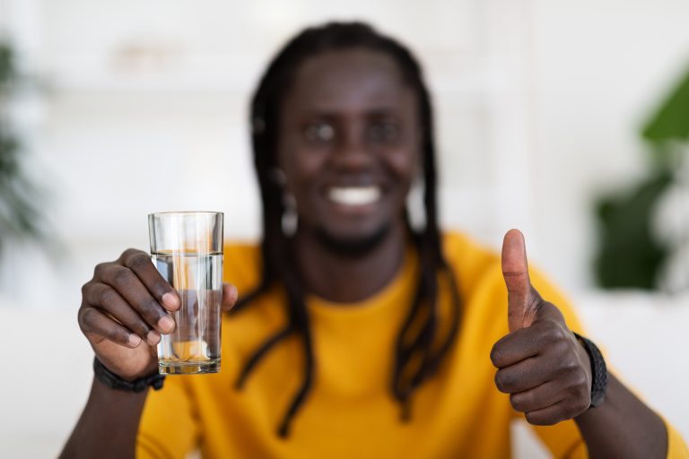 Smiling African American Male Holding Glass Of Water And Showing Thumb Up