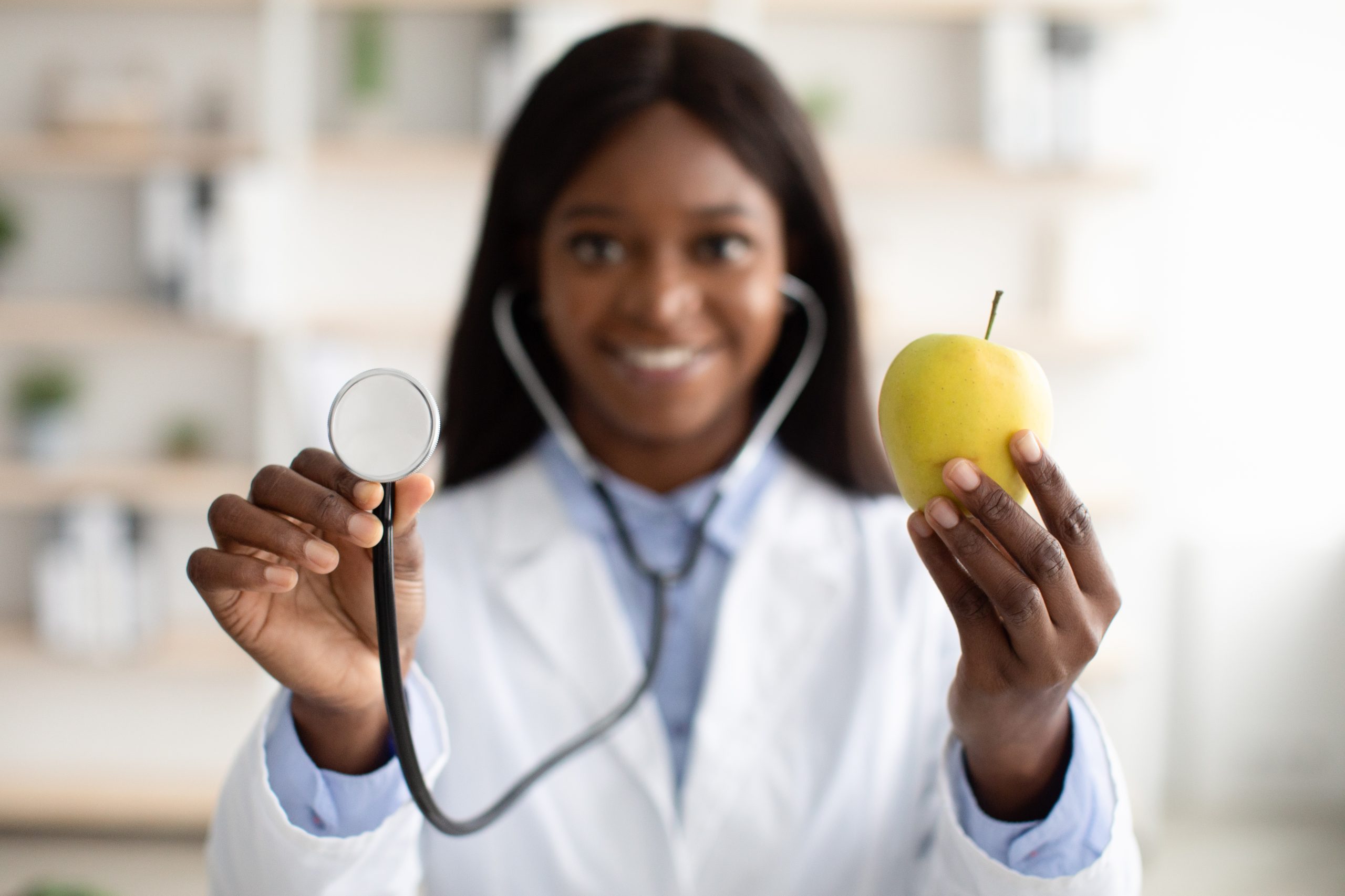 African american nutritionist showing organic green apple and using stethoscope, closeup