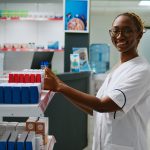 Smiling female pharmacist analyzing boxes of medicine on pharmacy shelves