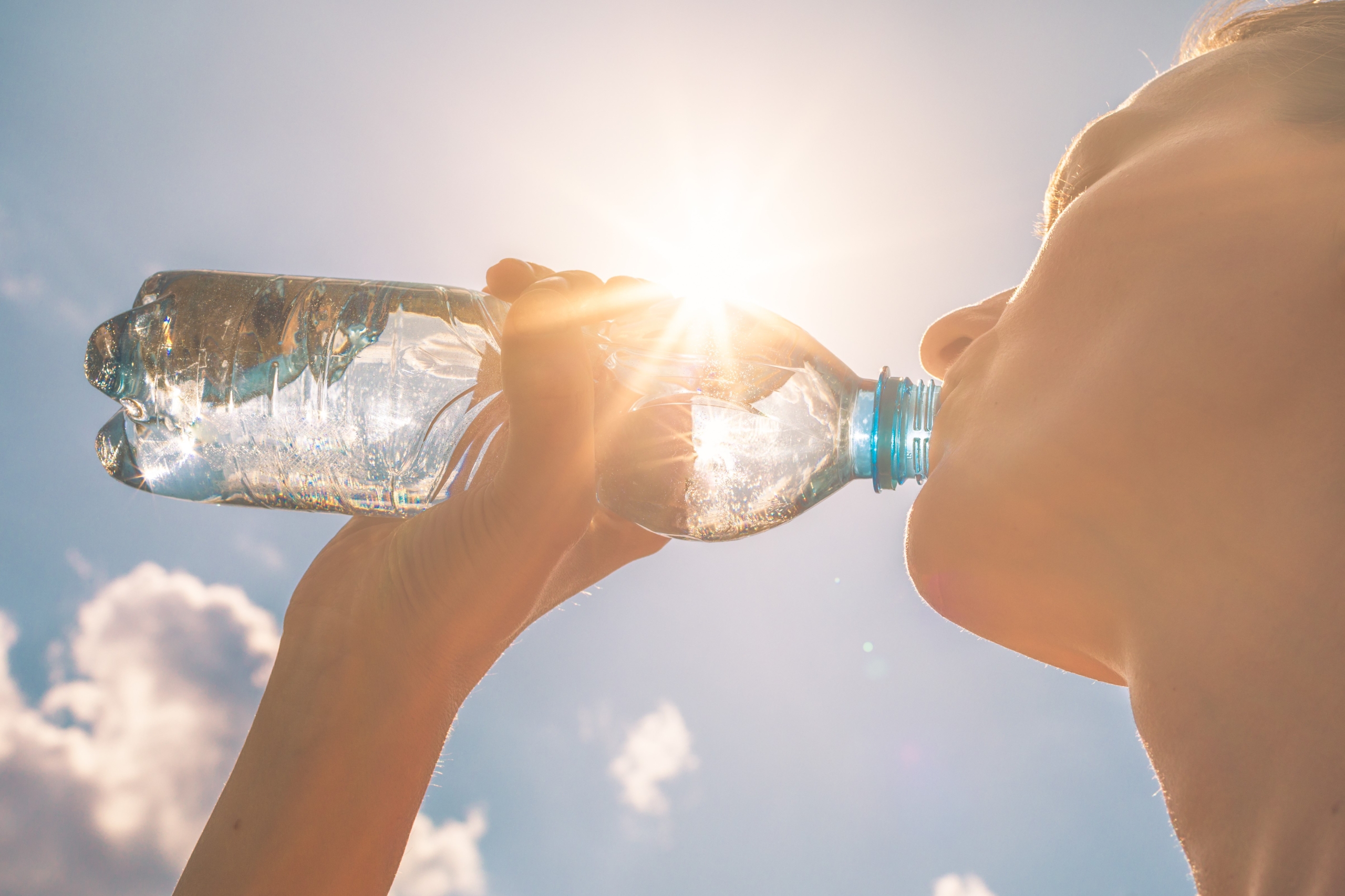 A person drinking water from a bottle against a sunny sky.