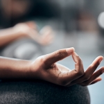 Close-up of a person's hand in a meditative mudra position, focusing on the thumb and index finger touching, with blurred background.