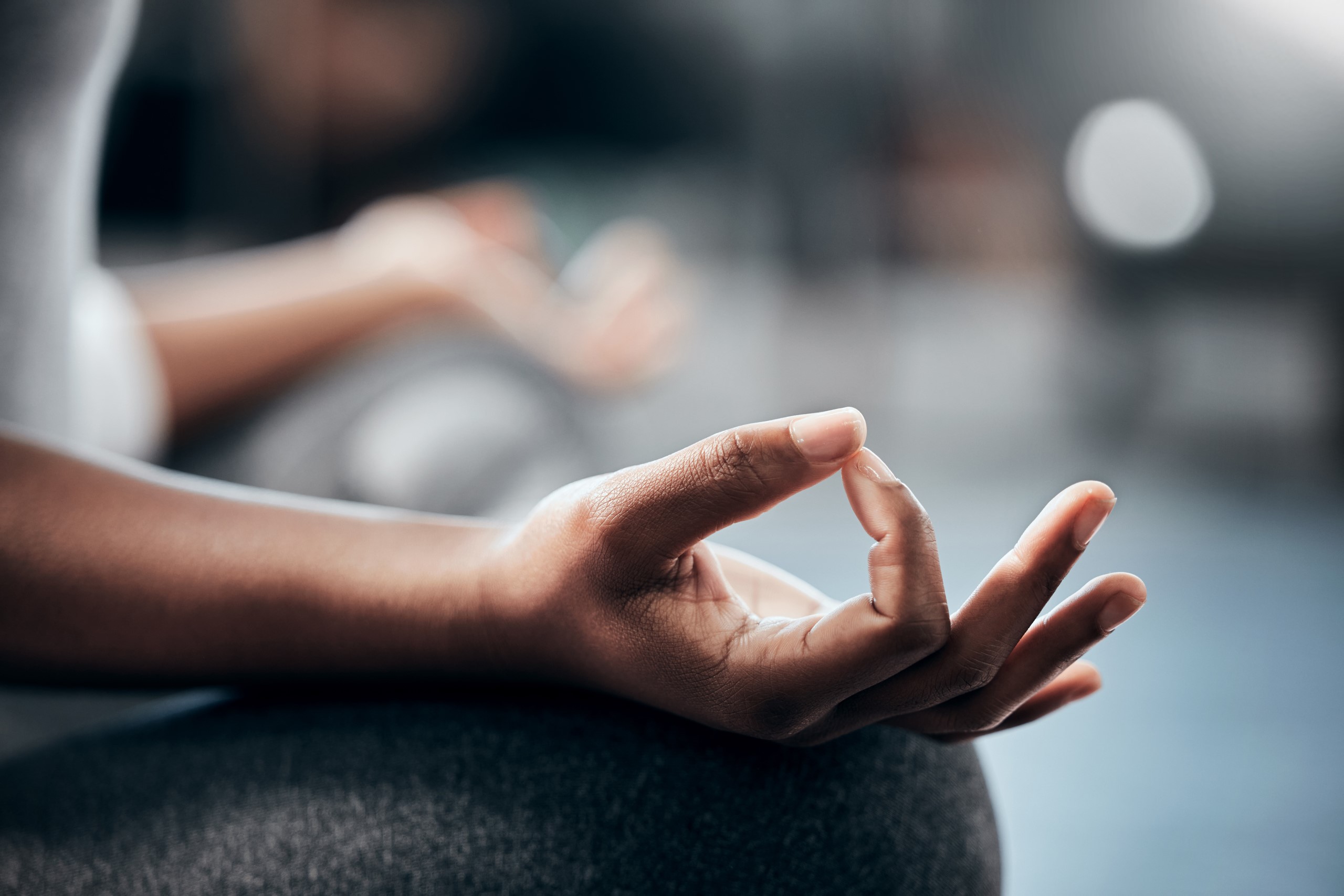 Close-up of a person's hand in a meditative mudra position, focusing on the thumb and index finger touching, with blurred background.