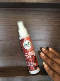 A hand holding a bottle of avon cuticle cleaner on a wooden surface.