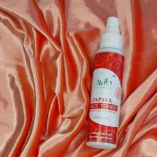 Bottle of avila papaya juice toner positioned on a ruffled coral silk fabric.