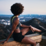 A woman stretching on a guardrail at dusk with a cityscape in the background, incorporating outdoor workouts into her routine.