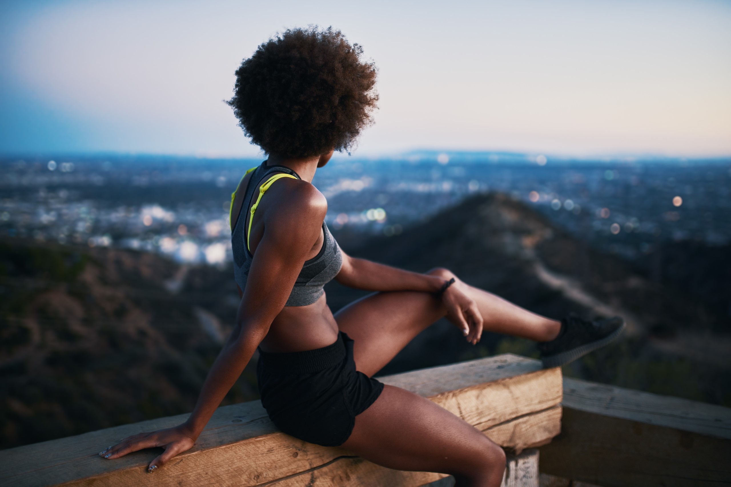 A woman stretching on a guardrail at dusk with a cityscape in the background, incorporating outdoor workouts into her routine.