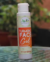 A bottle of avila naturalle turmeric face gel standing on a glass surface with greenery in the background.