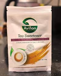 A white package of Avilan Naturals Tea Sweetener, noted to be rich in vitamin C, sits on a dark countertop.