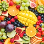 Assortment of fresh fruits including sliced oranges, mango, kiwi, figs, grapes, blueberries, raspberries, strawberries, and plums arranged on a surface.