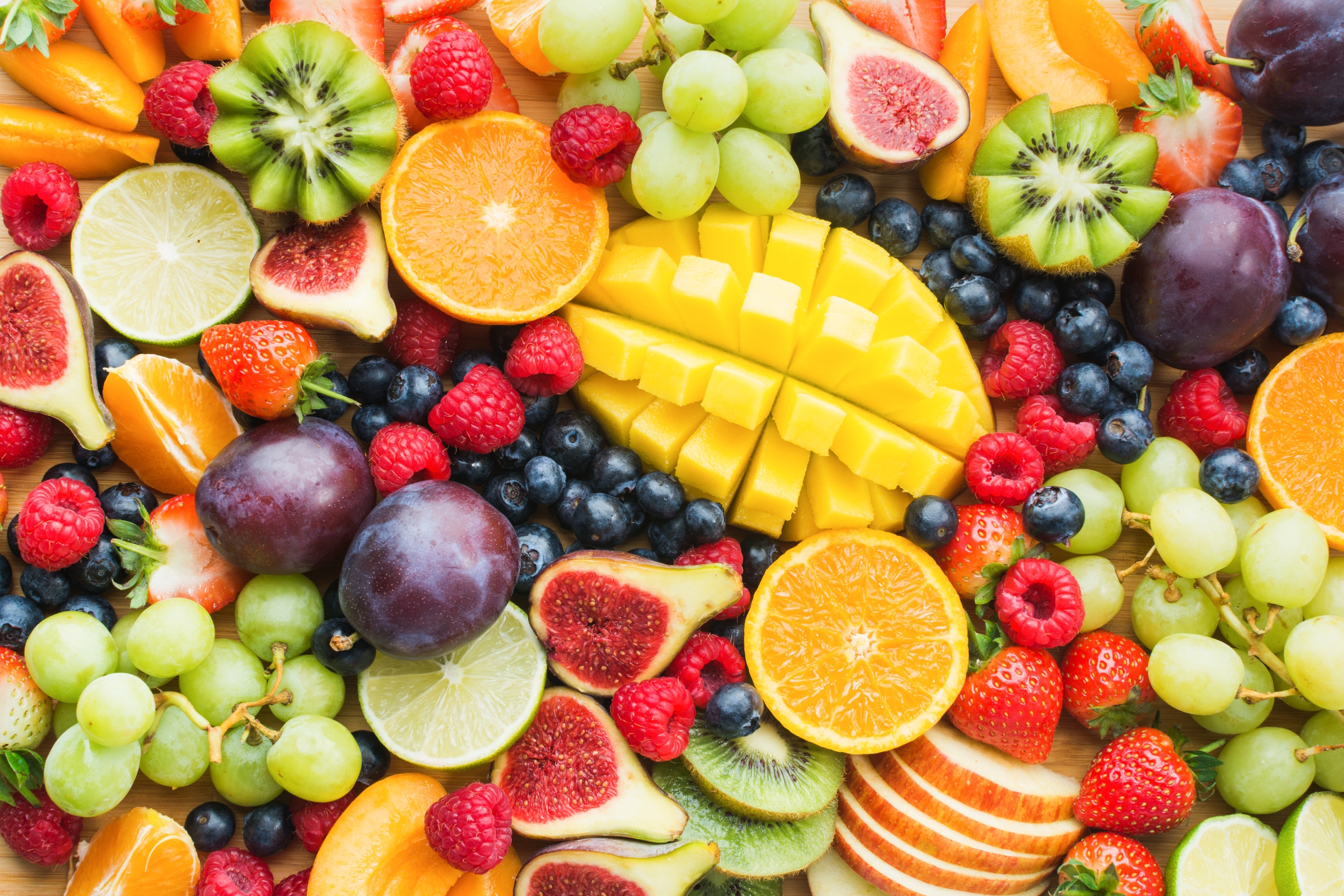 Assortment of fresh fruits including sliced oranges, mango, kiwi, figs, grapes, blueberries, raspberries, strawberries, and plums arranged on a surface.